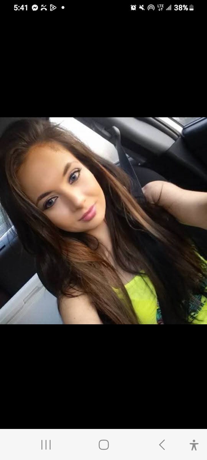 Jennifer Jorgensen Ahmed with long brown hair in a neon yellow top taking a car selfie